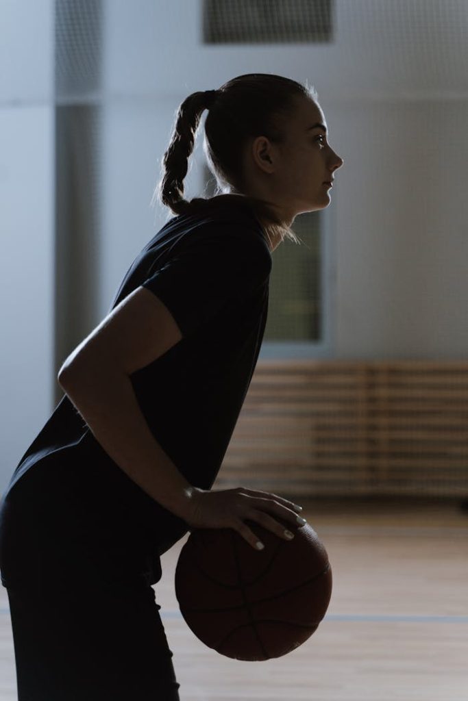 A woman basketball player in a focused pose on an indoor basketball court.